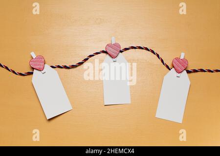 Minimalistic simple Valentine`s day concept, empty white cards for wishes with little red heart pins on beige wooden surface Stock Photo